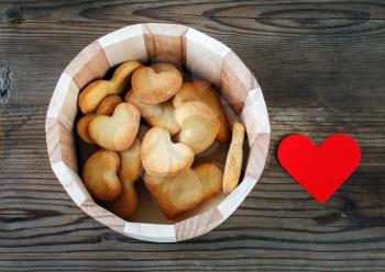 Heart-shaped cookies and red paper heart on a vintage wooden table background.