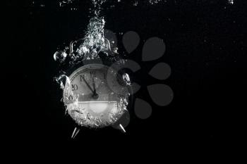 Alarm clock in water. Concept of time. Clock falls into the water with a splash and air bubbles. Plenty of space for text.