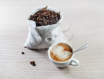 Espresso cup and coffee beans in a canvas bag against black wooden table background.