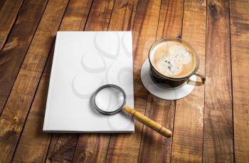 Blank closed book, magnifier and coffee cup on wooden background. Photo of stationery elements. Template for placing your design. Responsive design mockup.
