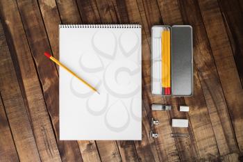 Photo of blank stationery set: album, pencil case, pencil, flash drive, clip, and eraser on wood table background. Template with plenty of copy space for placing your design. Top view