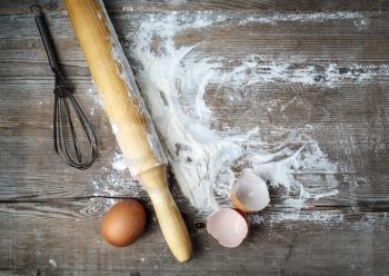 Still life with eggs, rolling pin, flour and whisk on vintage wood table background. Top view.