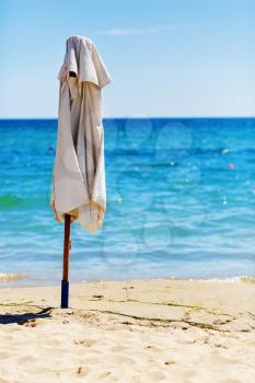 Folded beach umbrella against a blue sea and a cloudless sky on a sunny summer day. Selective focus.