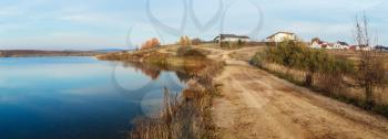 Country road along the shore of the lake. Autumn rural landscape. Panoramic shot.