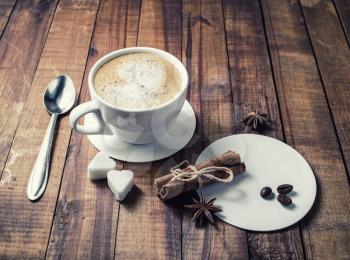 Delicious fresh coffee. Coffee cup with cinnamon sticks, coffee beans, anise, sugar, spoon and coasters on vintage wood kitchen table background.