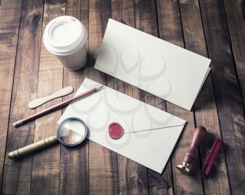 Photo of blank stationery set on wood table background. Blank envelope, postcard, magnifier, seal, stamp, pencil and coffee cup. Vintage still life with postal accessories. Top view.
