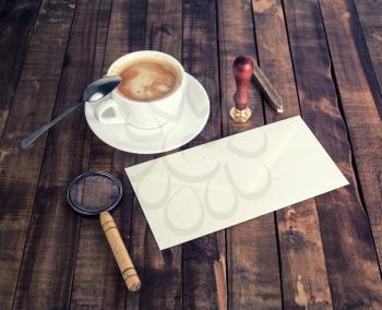 Photo of vintage stationery. Blank envelope, magnifier, seal, stamp, coffee cup and spoon on wooden background.