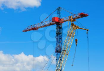 Two tower cranes against blue sky background.