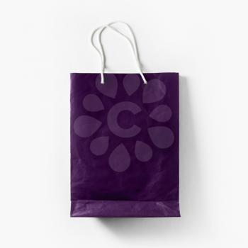 Blank violet paper shopping bag with white rope handles on white paper background. Top view. Flat lay.