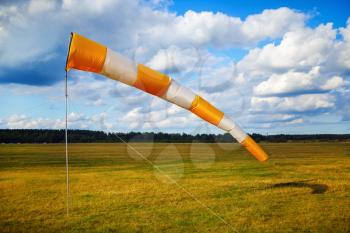 Windsock at small airfield. Blue sky with clouds and field of grass.