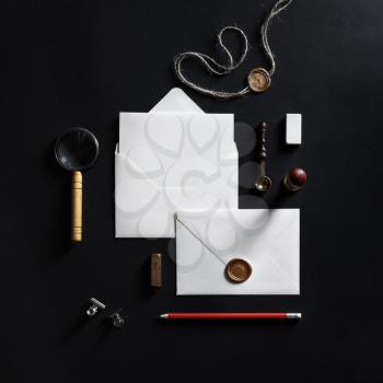 Blank white paper envelopes with wax seal stamp and stationery on black paper background. Flat lay.