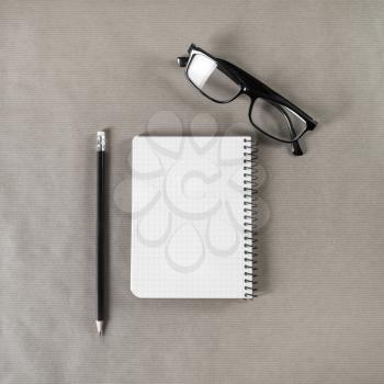 Blank notebook, glasses and pencil on craft paper background. Mock up for graphic designers portfolios. Stationery template. Top view.