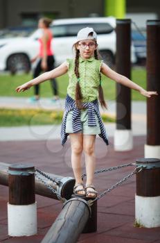 Little girl walking on a log in the playground. Child balancing on a log. Selective focus.