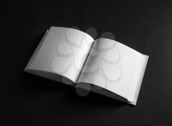 Open blank square book on black paper background.
