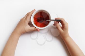 Child stirs sugar in cup of tea over white background.