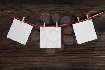 Blank photo paper attach to rope with clothespins on wooden background. Template for placing your design.