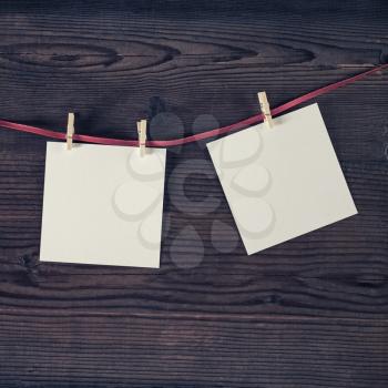 Blank white photo frames hanging with clothespins on vintage wood background.