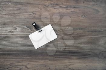 Blank badge mockup on wood table background. White plastic id card. Space for text. Flat lay.