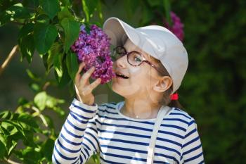 Child girl smelling lilac flowers in the garden. Selective focus.