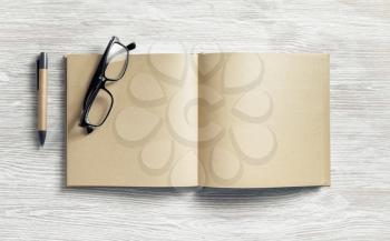 Photo of blank notepad with blank kraft paper pages, pen and glasses on light wood table background. Flat lay.