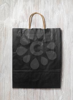 Black paper bag on light wood table background. Responsive design mockup. Flat lay.