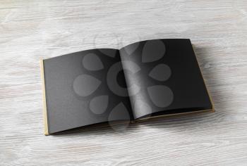 Opened book with blank black pages on light wooden background.
