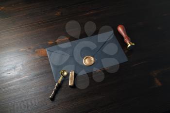 Blank black paper envelope with golden wax seal, stamp and spoon on wood table background. Mockup for your design.
