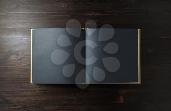 Opened blank black book on wooden background. Top view. Flat lay.