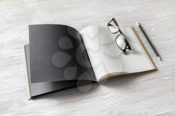 Blank open book, glasses and pencil on wood table background. Responsive design mockup.