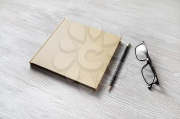 Photo of closed blank square book, glasses and pencil on wooden background. Template for placing your design.