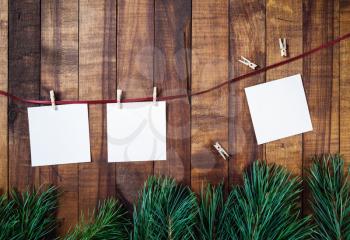 Blank notes or photos, clothespins, rope and pine branches on wooden background. Stationery template. Flat lay.
