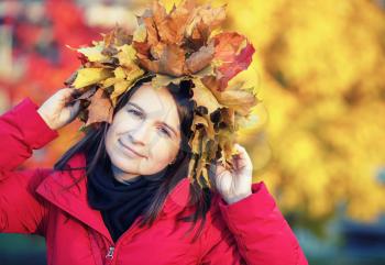 Pretty young woman with with a wreath of autumn maple leaves. Girl in autumn. Selective focus on model. Toned image.