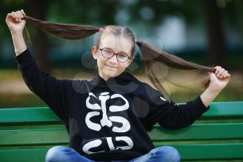Girl with hairstyle ponytails sitting on a bench. Child with long hair. Selective focus.