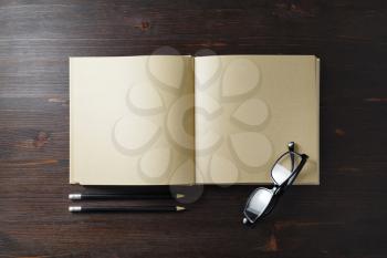 Blank kraft paper book, glasses and pencils on wood table background. Responsive design template. Flat lay.