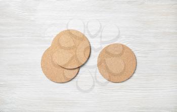 Photo of three blank cork beer coasters on light wooden background. Flat lay.