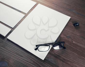 Photo of blank stationery set on wood background. Blank stationery and corporate identity template. Blank letterhead, glasses, sharpener and paper.