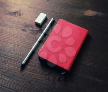 Red notepad, pencil and eraser on dark wood table background.