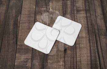 Blank white square beer coasters on wooden background.