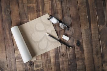 Blank notepad or brochure of kraft paper and stationery: glasses, pencil and eraser on vintage wooden background. Responsive design mockup. Flat lay.