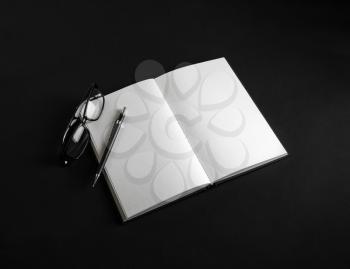 Photo of blank book, pencil and glasses on black background.