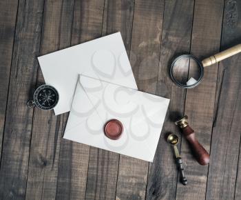 Blank envelope and stationery: wax seal, stamp, spoon, magnifier, compass and postcard on wooden background. Flat lay.