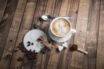 Coffee and spices. Coffee cup, cinnamon sticks, coffee beans, anise, sugar, spoon and beer coasters on wood table background.