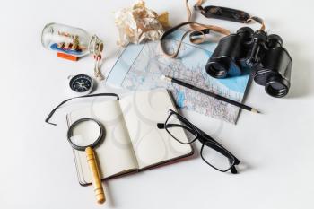 Travel and tourism still life. Map, binoculars, compass, notepad, magnifier, glasses, pencil and crumpled paper on white paper background.