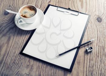Photo of clipboard with a blank sheet of paper, coffee cup, pencil and sharpener on wooden background with plenty of copy space. Blank branding mock-up.