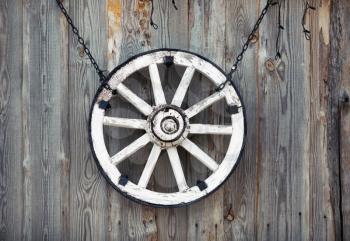 Old cart wheel hanging on vintage wooden wall.