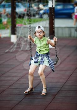 Child girl is swinging on a swing on the playground. Selective focus.