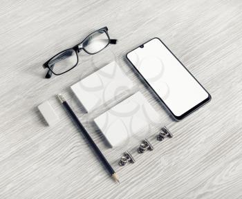 Blank stationery template on light wood table background. Smartphone, business cards, pencil, eraser and glasses.
