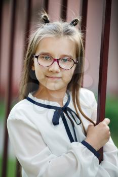 Child girl near the fence. Schoolgirl with glasses looking at the camera. Vertical shot. Selective focus.