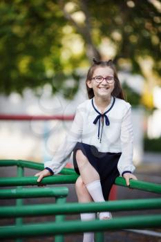 Smiling child girl sitting on the horizontal bar. Schoolgirl at the playground. Vertical shot. Selective focus.