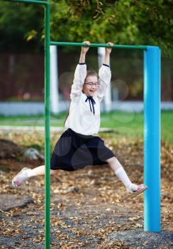 Happy schoolgirl hangs on the horizontal bar. Child girl having fun on the playground. Vertical shot. Selective focus.